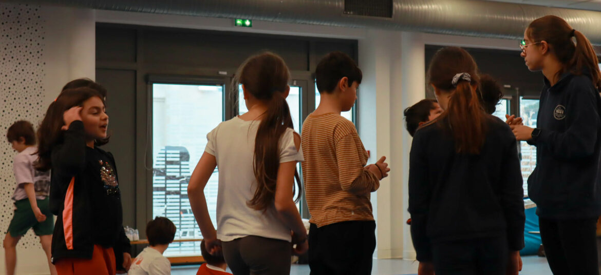 Enfants de 6 à 11 ans rassemblés en cercle avec une animatrice dans une salle de sport, en pleine discussion avant une activité ludique.