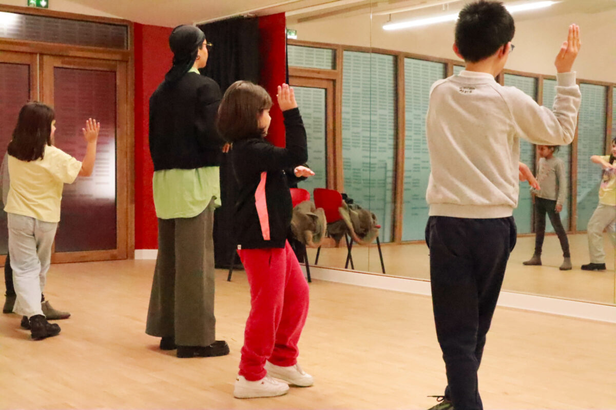Un groupe d'enfants accompagné d'une adulte pratique une chorégraphie devant un miroir dans une salle de danse.