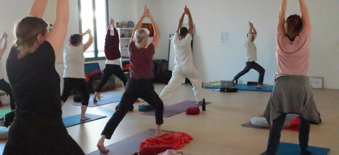 Professeur de yoga guidant un groupe d’élèves en posture dans une salle lumineuse.