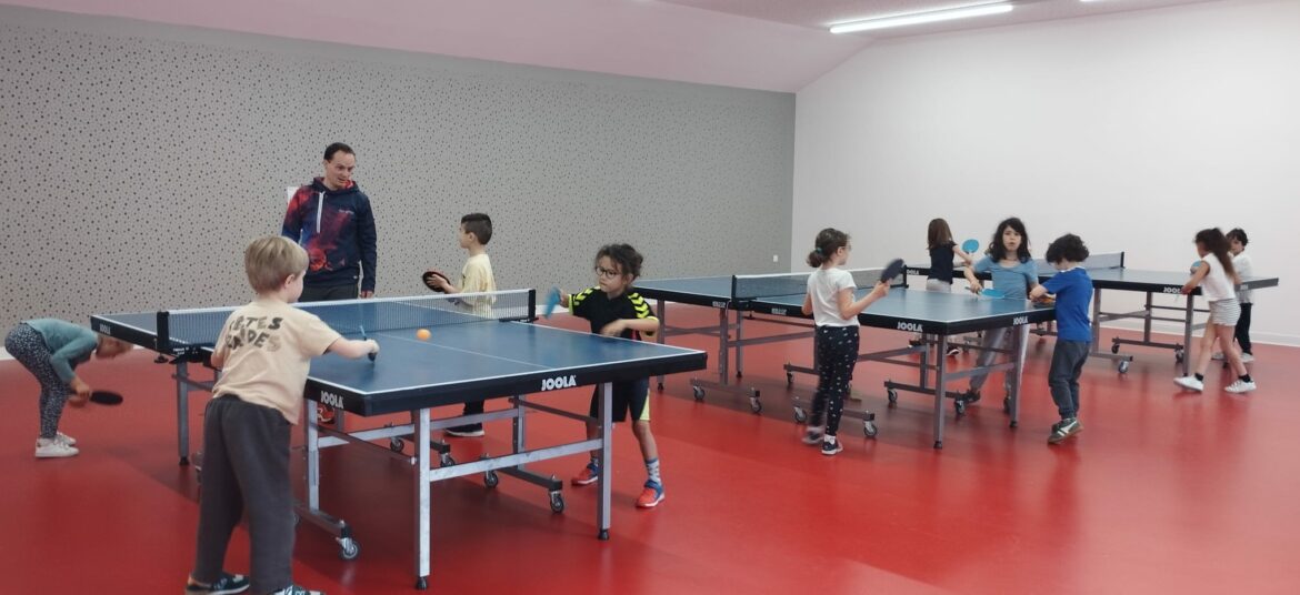 Groupe d'enfants jouant au tennis de table dans une salle d'entraînement encadrés par un éducateur.