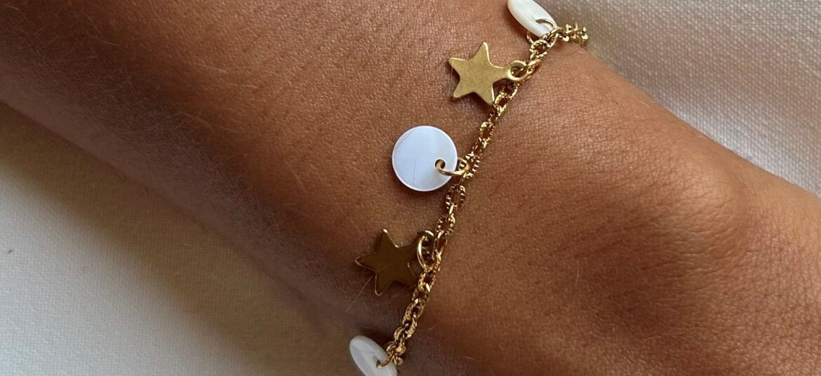 Un bracelet doré délicat orné de petites étoiles et de perles blanches porté au poignet.