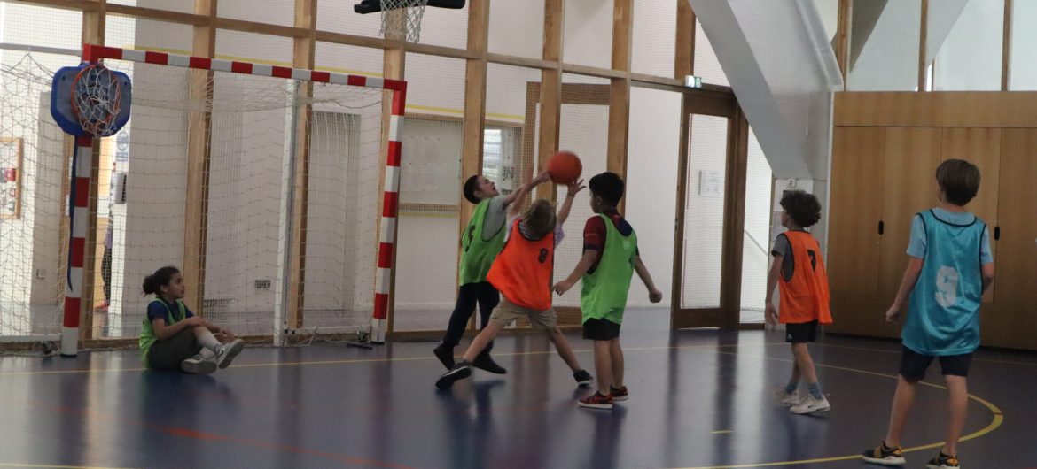 Match de basket en herbe Enfants disputant une partie de basket-ball en salle, en tenue de couleur pour différencier les équipes.