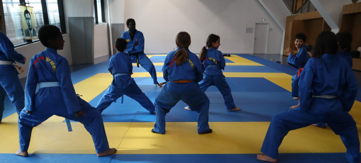 Cours de Vovinam Viet Vo Dao pour enfants Enfants en tenue bleue de Vovinam Viet Vo Dao effectuant un exercice collectif sur tatami, guidés par leur professeur.