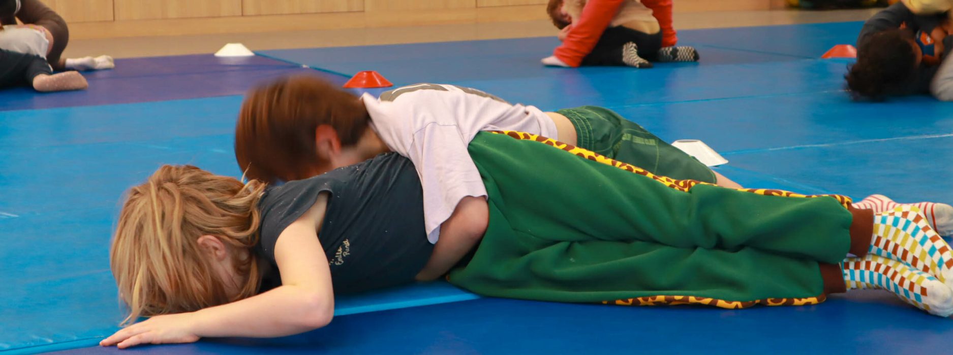 Des enfants pratiquant des exercices de judo au sol dans une salle de sport